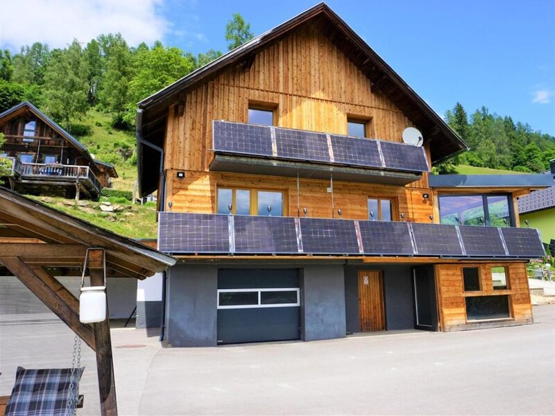 Die Wind Buam Hütte mit einer modernen Holzfassade, Solarmodulen an den Balkonen und umgeben von grüner Natur.