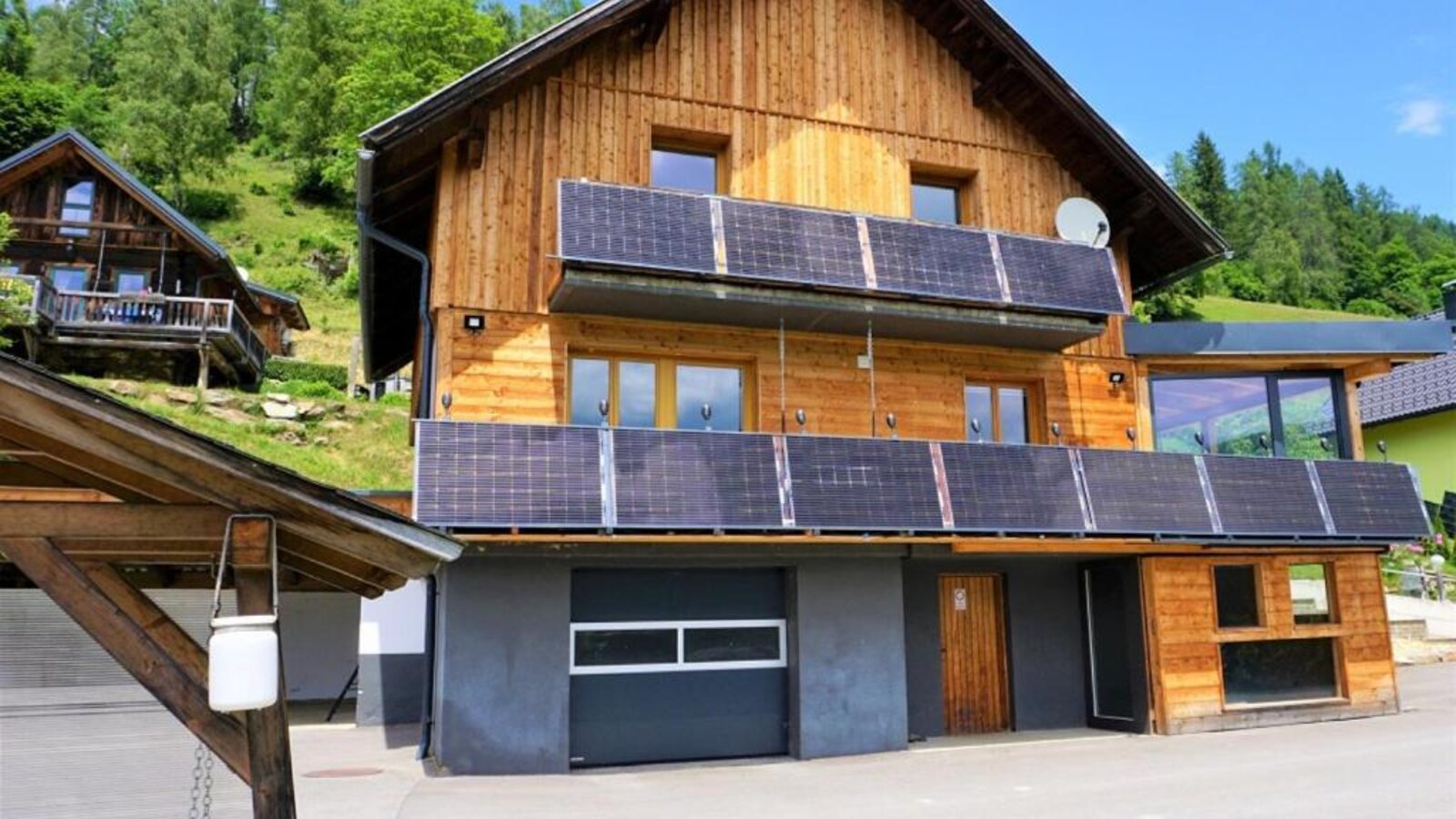 Die Wind Buam Hütte mit einer modernen Holzfassade, Solarmodulen an den Balkonen und umgeben von grüner Natur.
