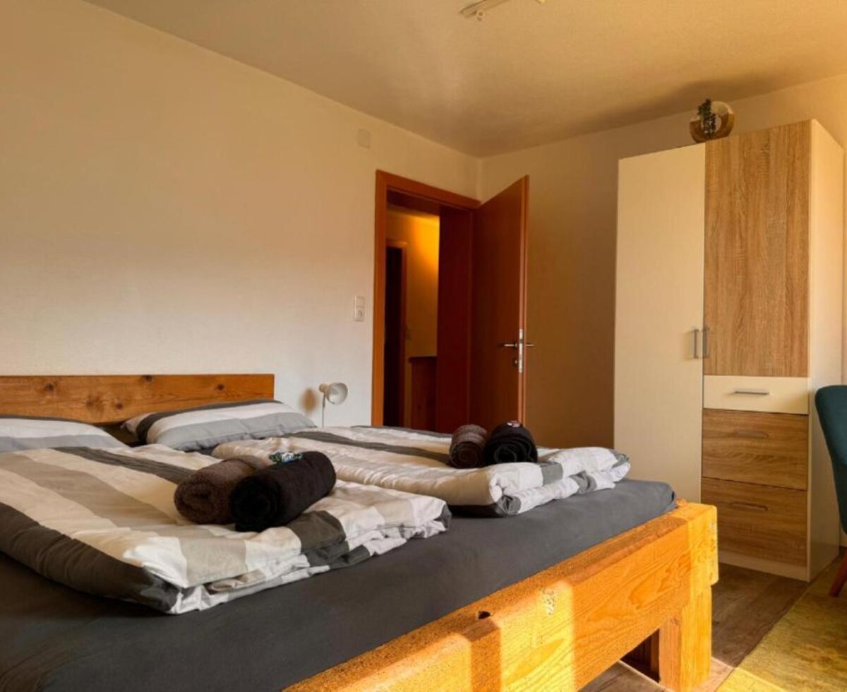 Ein gemütliches Doppelzimmer in der Wind Buam Hütte mit einem rustikalen Holzbett, frischen Handtüchern und einem hellen Kleiderschrank.