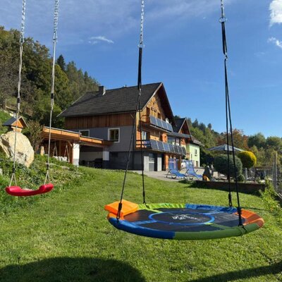 Der einladende Garten der Wind Buam Hütte mit einer sonnigen Wiese und bunten Kinderschaukeln.