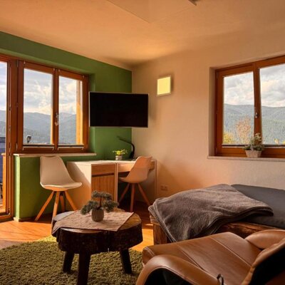 Ein einladender Wohnbereich in der Wind Buam Hütte mit einem bequemen Ledersessel, einem kleinen Schreibtisch und malerischem Ausblick auf die Berge.