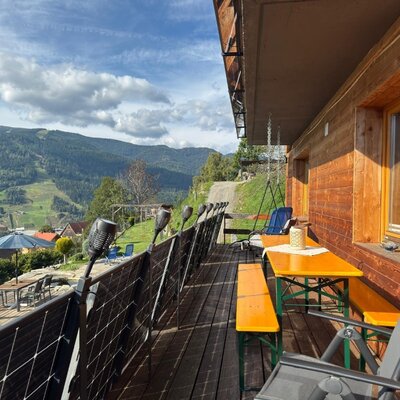 Die sonnige Holzterrasse der Wind Buam Hütte bietet gemütliche Sitzgelegenheiten und einen weiten Ausblick auf die malerische Bergkulisse.