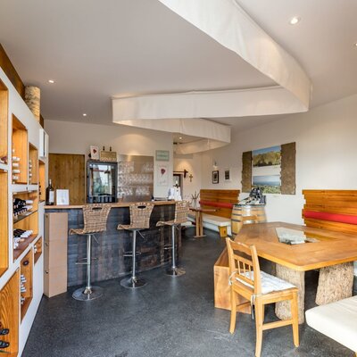 Der Verkostraum des Hauses mit Bar, Barhockern, Weinregalen und einem großen Holztisch mit Bänken.