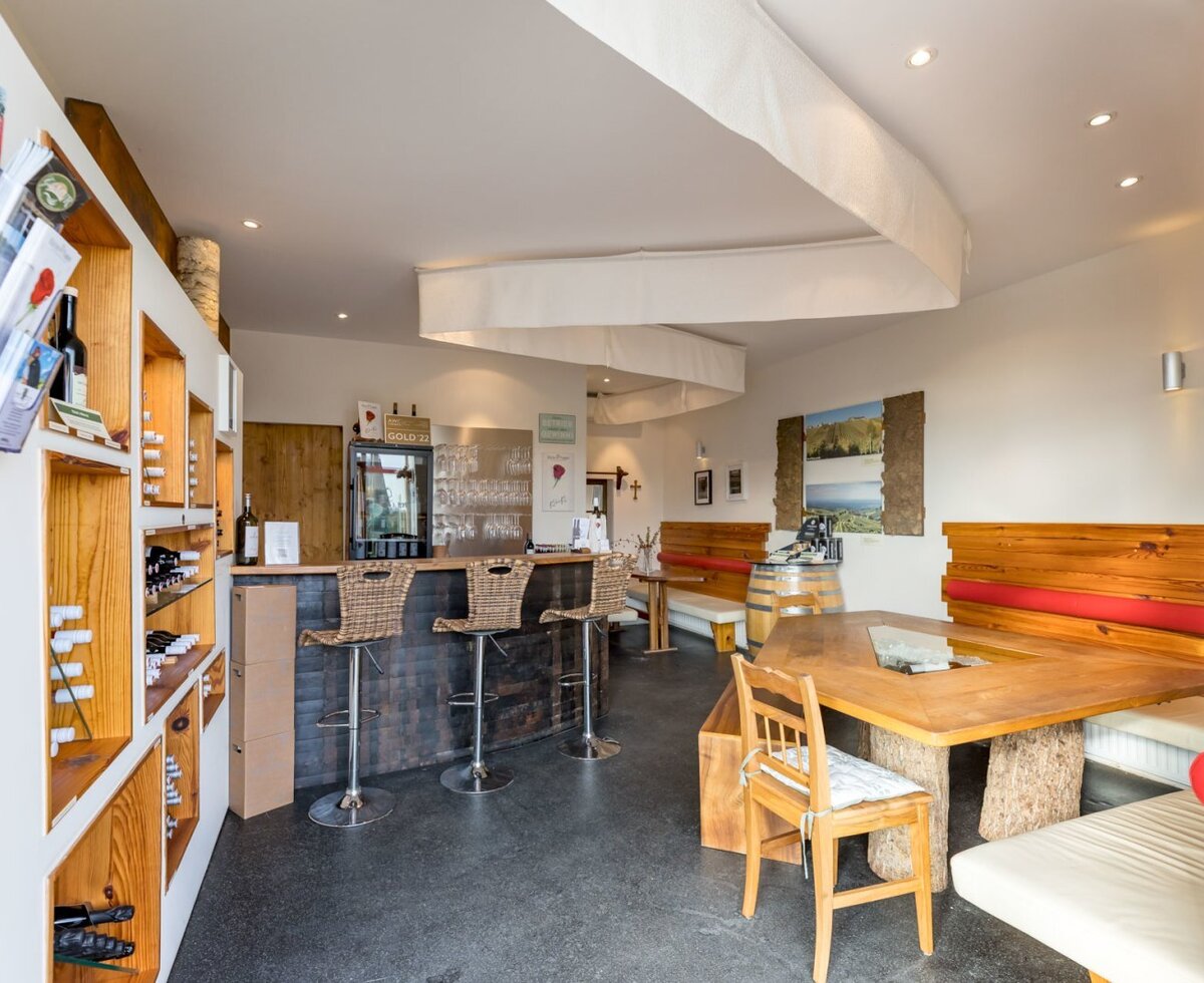 Der Verkostraum des Hauses mit Bar, Barhockern, Weinregalen und einem großen Holztisch mit Bänken.