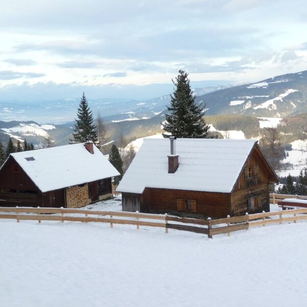 Der Hof mit dem Hauptgebäude und dem Nebengebäude mit Sauna, beide mit schneebedeckten Dächern, in einer verschneiten Berglandschaft.