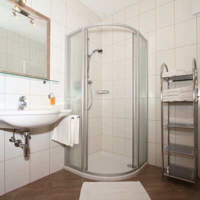 Badezimmer im Bauernhof mit Dusche, Waschbecken, Spiegel, Haarföhn und Handtuchheizkörper.