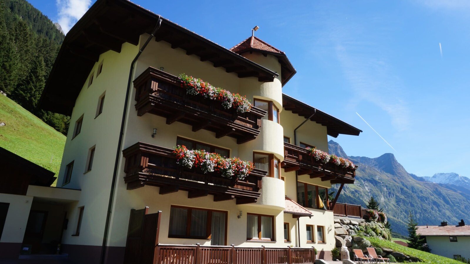 Außenansicht des Bauernhofs mit Balkonen, Blumenkästen und Blick auf die Pitztaler Bergwelt.