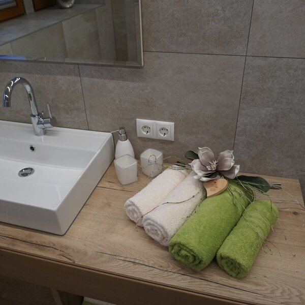 Badezimmer im Bauernhof mit einem Waschbecken auf einem Holzwaschtisch, einem Spiegel und frischen Handtüchern.