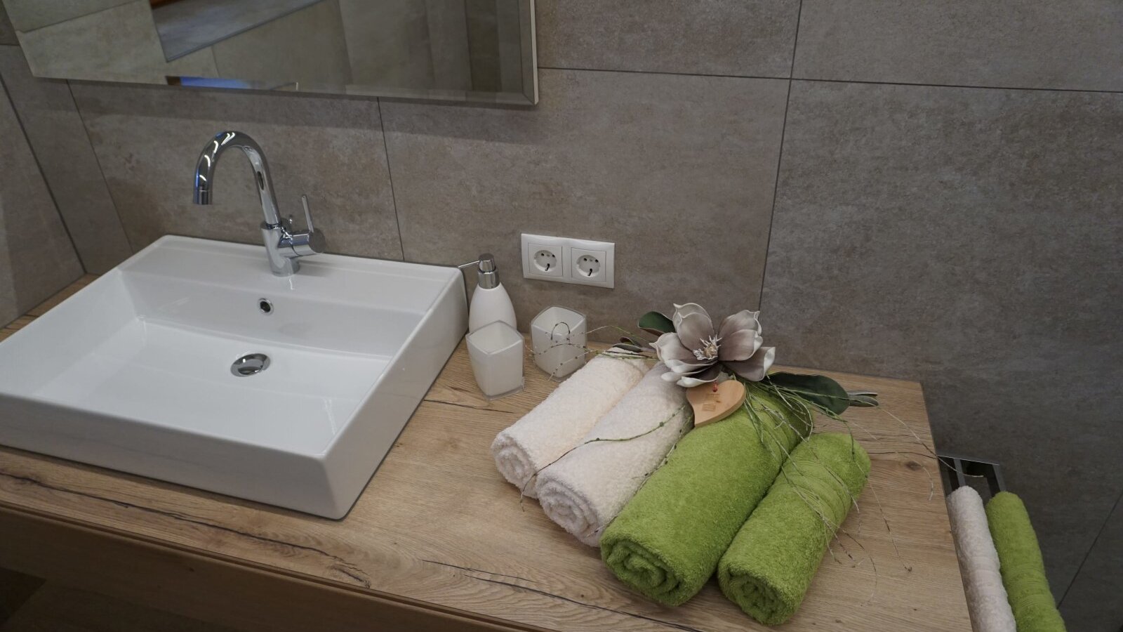 Badezimmer im Bauernhof mit einem Waschbecken auf einem Holzwaschtisch, einem Spiegel und frischen Handtüchern.