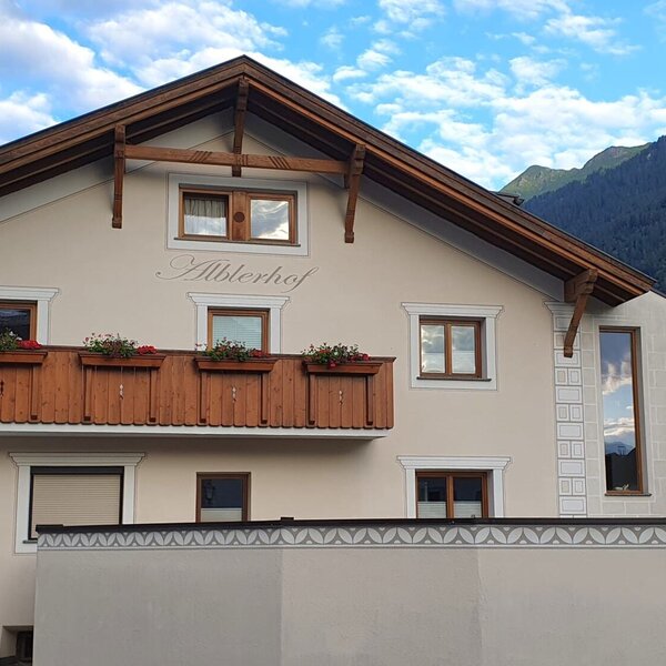 Die Außenansicht des Bauernhofs Alblerhof mit traditioneller Architektur, einem Holzbalkon mit Blumenkästen und Bergblick.