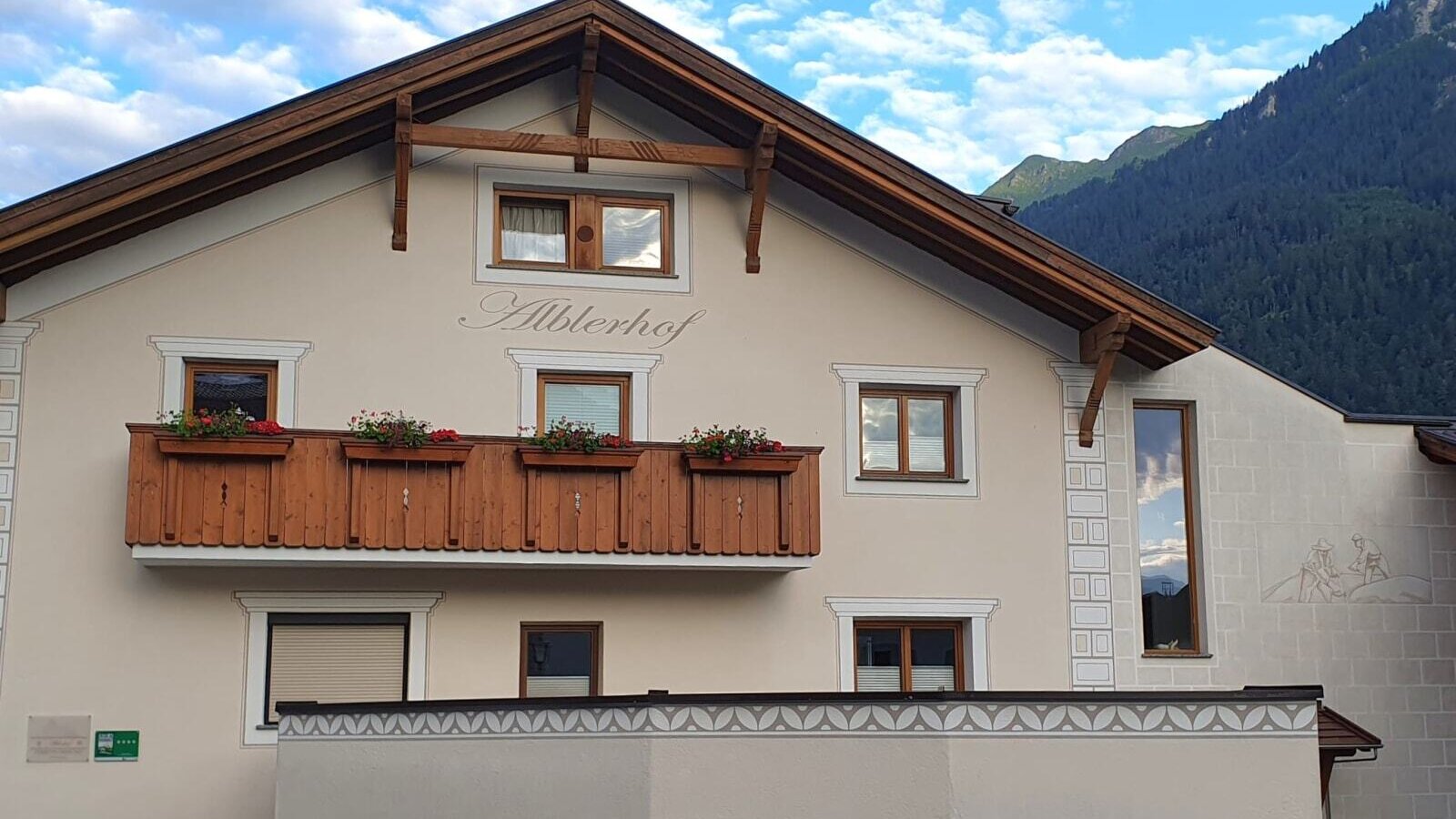 Die Außenansicht des Bauernhofs Alblerhof mit traditioneller Architektur, einem Holzbalkon mit Blumenkästen und Bergblick.
