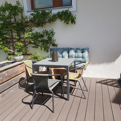 Terrasse des Bauernhofs mit einem Esstisch, vier Stühlen und einer Sitzbank, umgeben von Pflanzen.