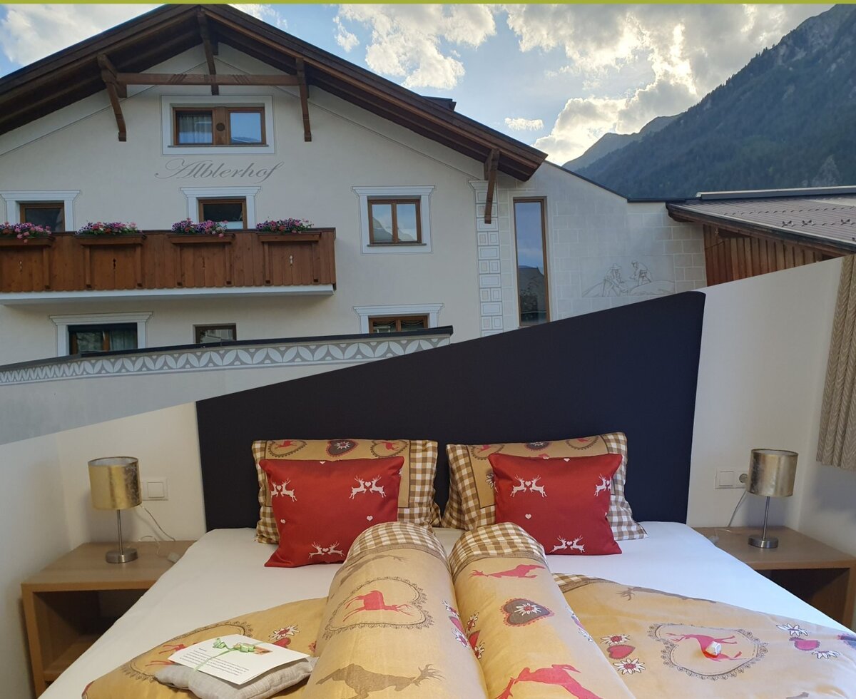 Schlafzimmer im Bauernhof mit Doppelbett, Nachttischen, Leselampen und Blick auf den Alblerhof und die Berge.