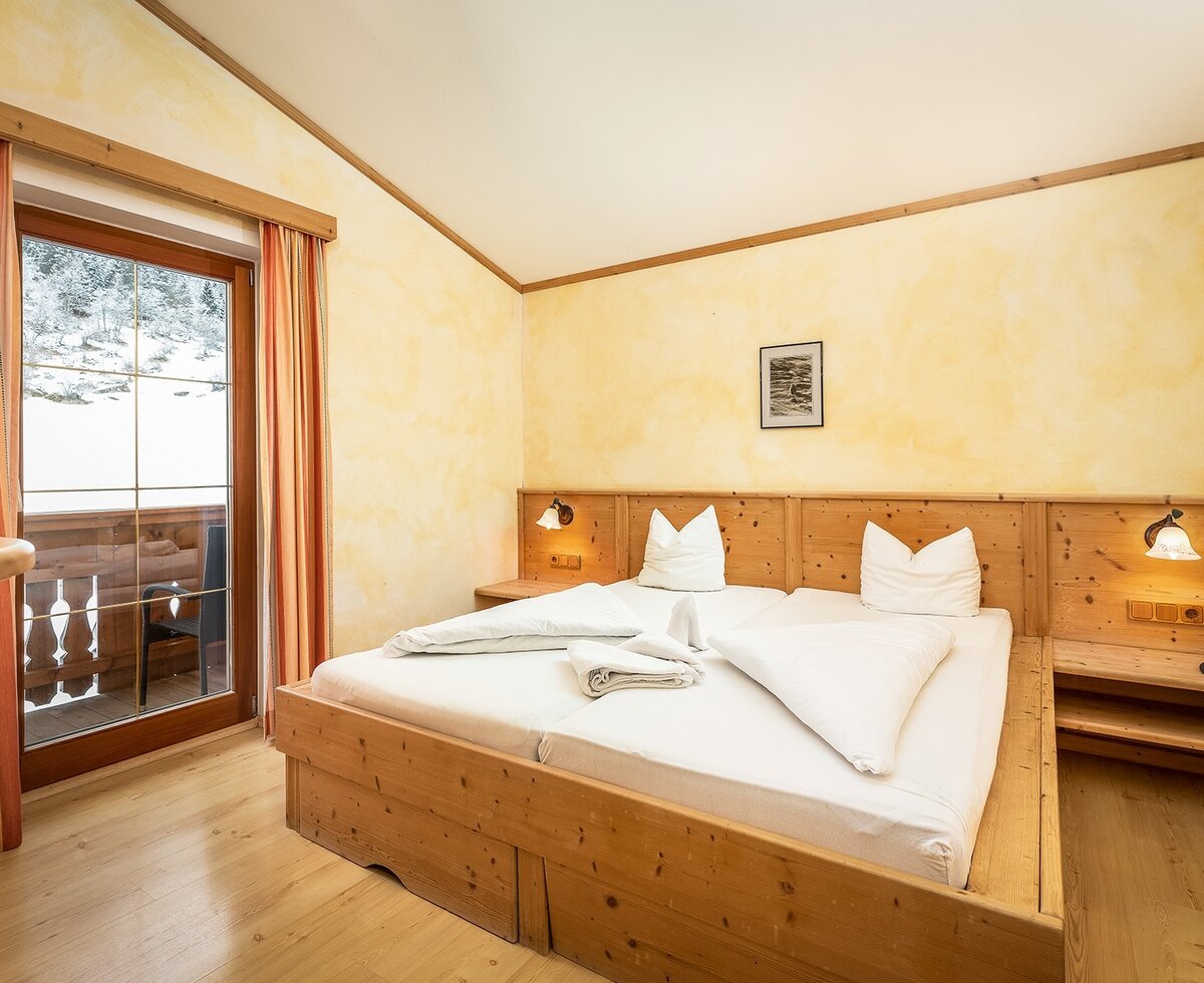 Doppelzimmer im Bauernhof mit Holzmöbeln, Telefon und Balkon mit Blick auf die verschneite Landschaft.