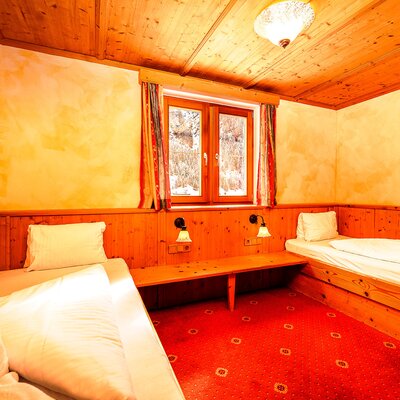 Schlafzimmer im Bauernhof mit zwei Einzelbetten, Holzvertäfelung und Blick durch das Fenster.
