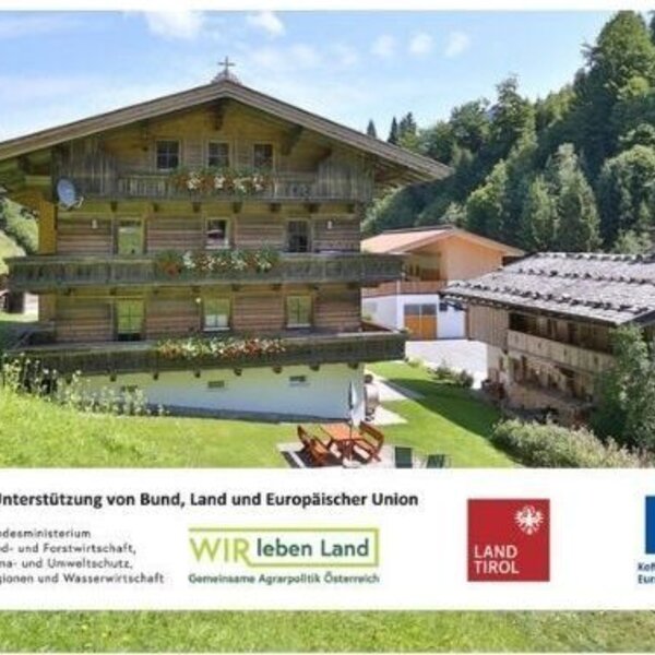 Der einladende Bauernhof inmitten grüner Bergwiesen mit traditionellen Holzbalkonen und einem gepflegten Gartenbereich.