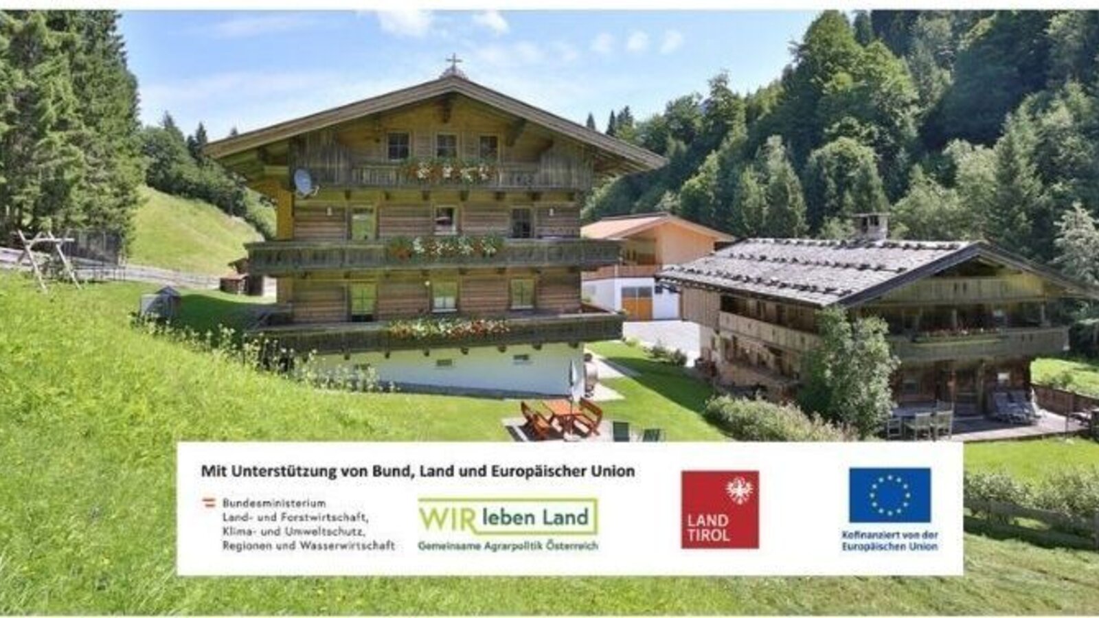 Der einladende Bauernhof inmitten grüner Bergwiesen mit traditionellen Holzbalkonen und einem gepflegten Gartenbereich.