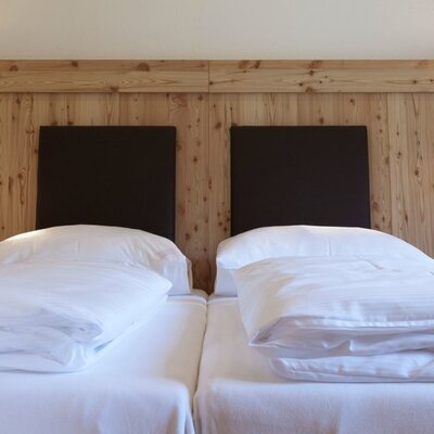 Einladendes Doppelbett im Appartement mit weicher weißer Bettwäsche, einer rustikalen Holzrückwand und gemütlicher Beleuchtung.