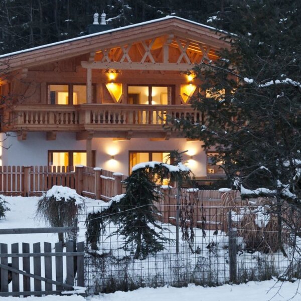 Das charmante Appartement-Haus in einer verschneiten Winterlandschaft, warm beleuchtet am Abend.