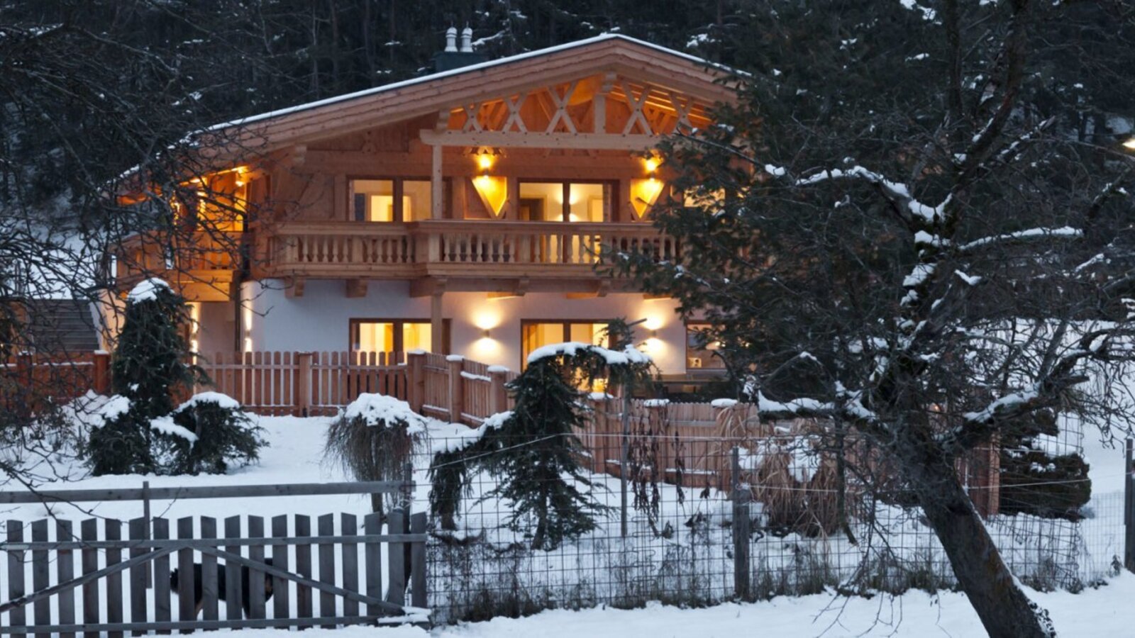 Das charmante Appartement-Haus in einer verschneiten Winterlandschaft, warm beleuchtet am Abend.