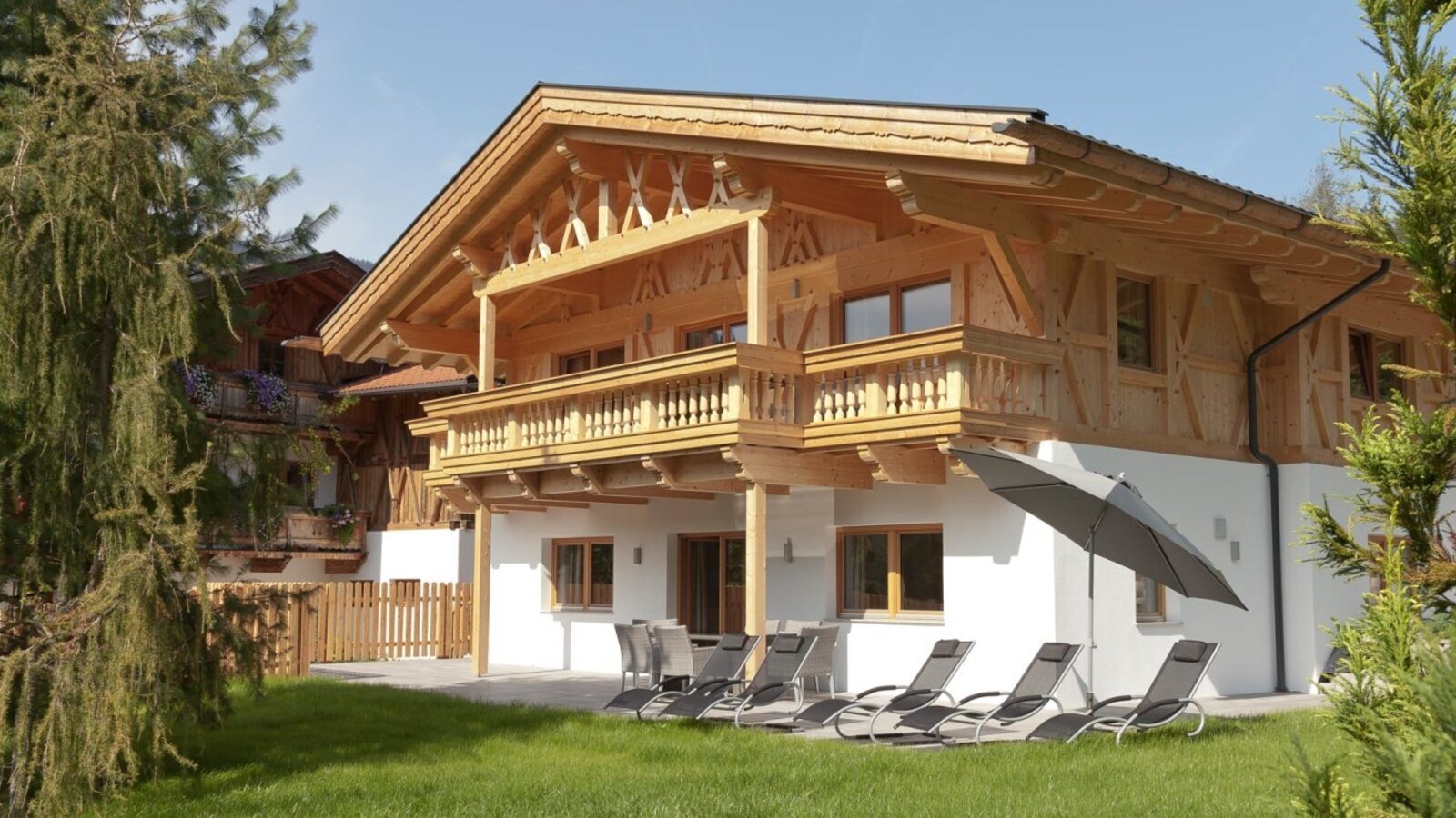 Die einladenden Appartements mit Holzfassade, sonniger Terrasse und gemütlichen Liegestühlen im grünen Garten.