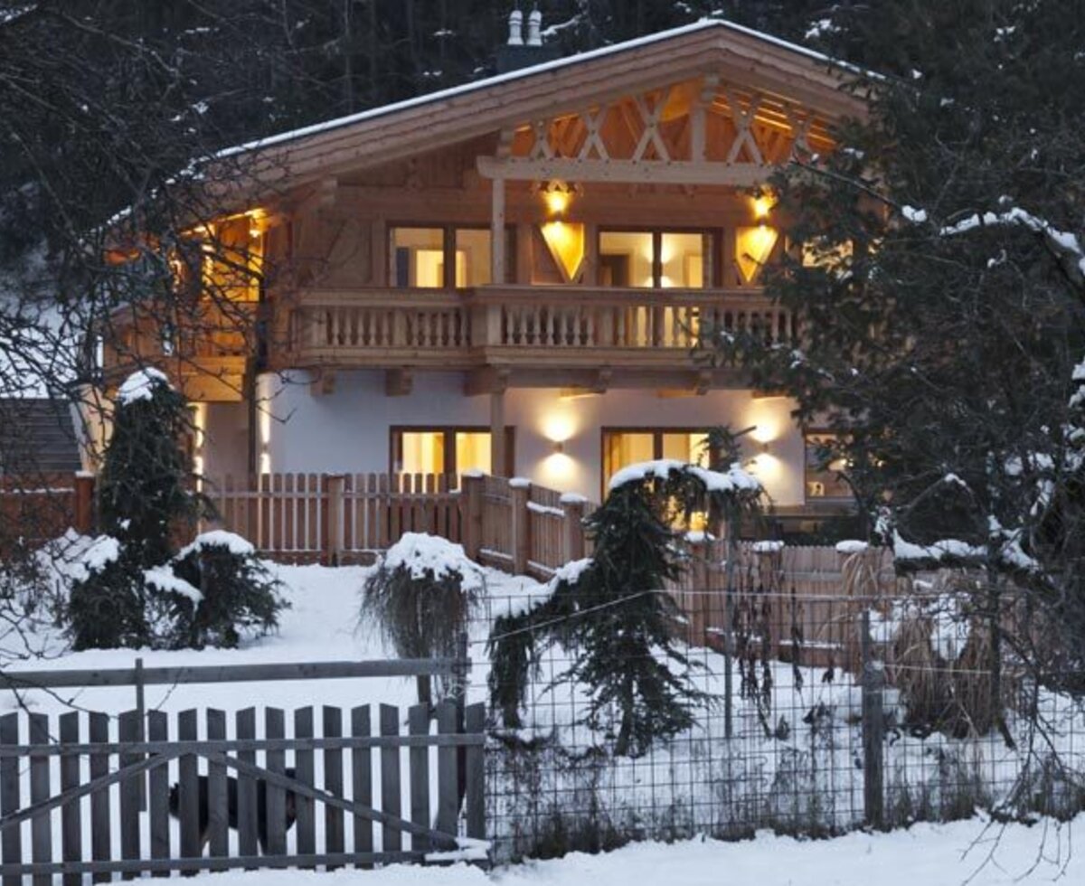 Das einladende Appartements-Haus in einer verschneiten Winterlandschaft, warm erleuchtet in der Abenddämmerung.