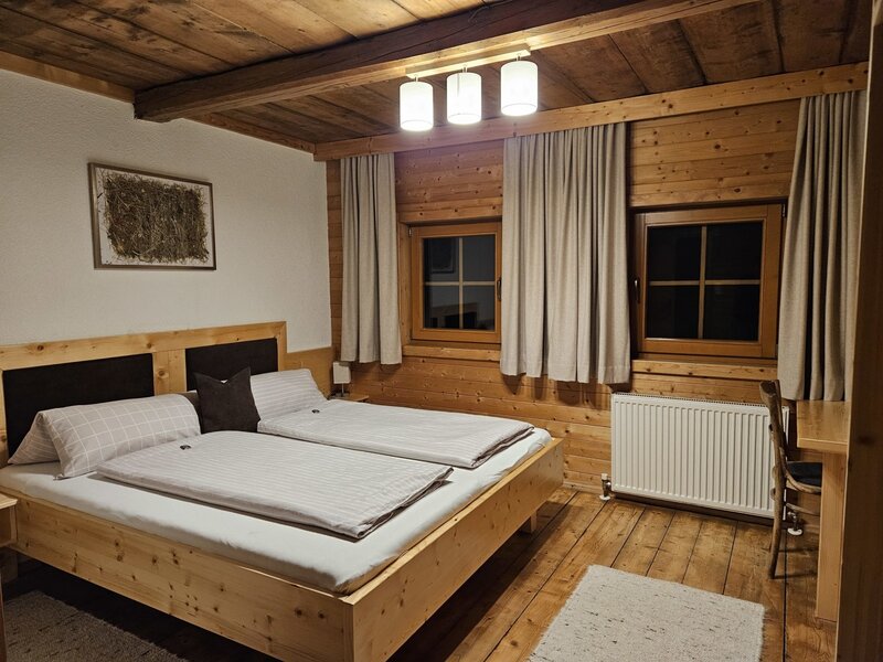 Doppelzimmer im Bauernhof mit Holzbett, Holzwänden, Holzbalkendecke und Schreibtisch.