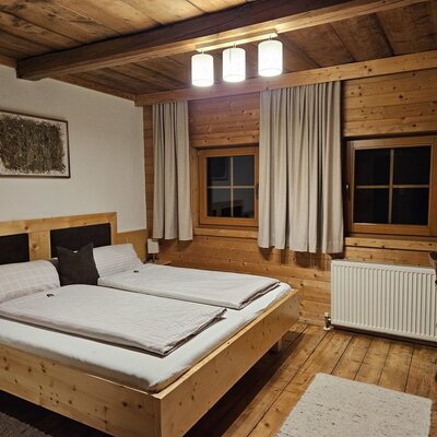 Doppelzimmer im Bauernhof mit Holzbett, Holzwänden, Holzbalkendecke und Schreibtisch.