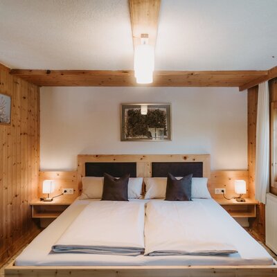 Doppelzimmer im Bauernhof mit Holzvertäfelung, Doppelbett, Nachttischen und Fenster.