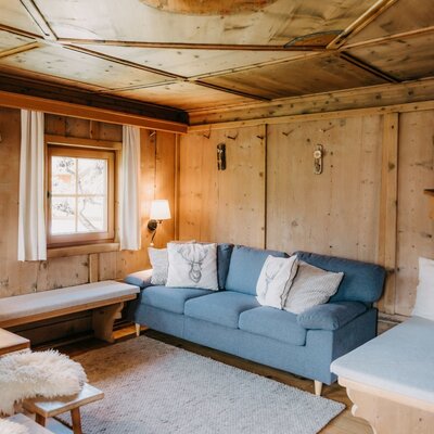 Holzgetäfeltes Zimmer im Bauernhof mit Sofa, Holztisch, Sitzbänken und Fenster.