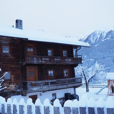 Der winterliche Bauernhof mit Balkonen, einem Kinderspielplatz und Blick auf die schneebedeckten Berge.