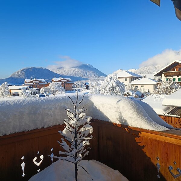 Blick vom Südbalkon des Bauernhofs auf die verschneite Winterlandschaft mit Dorf und Bergen.