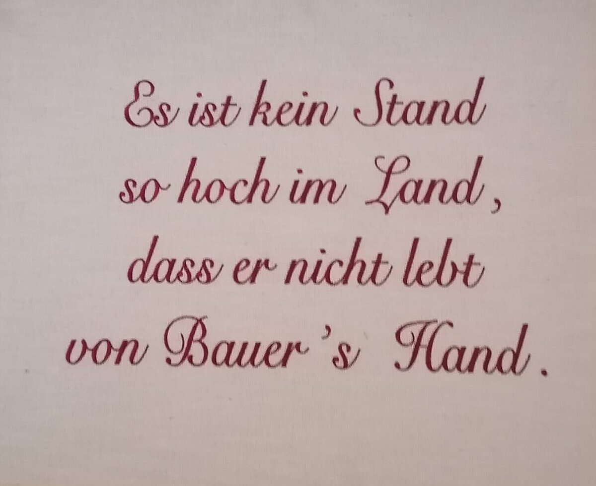 Eine Wanddekoration auf dem Bauernhof mit dem deutschen Spruch „Es ist kein Stand so hoch im Land, dass er nicht lebt von Bauer’s Hand.“