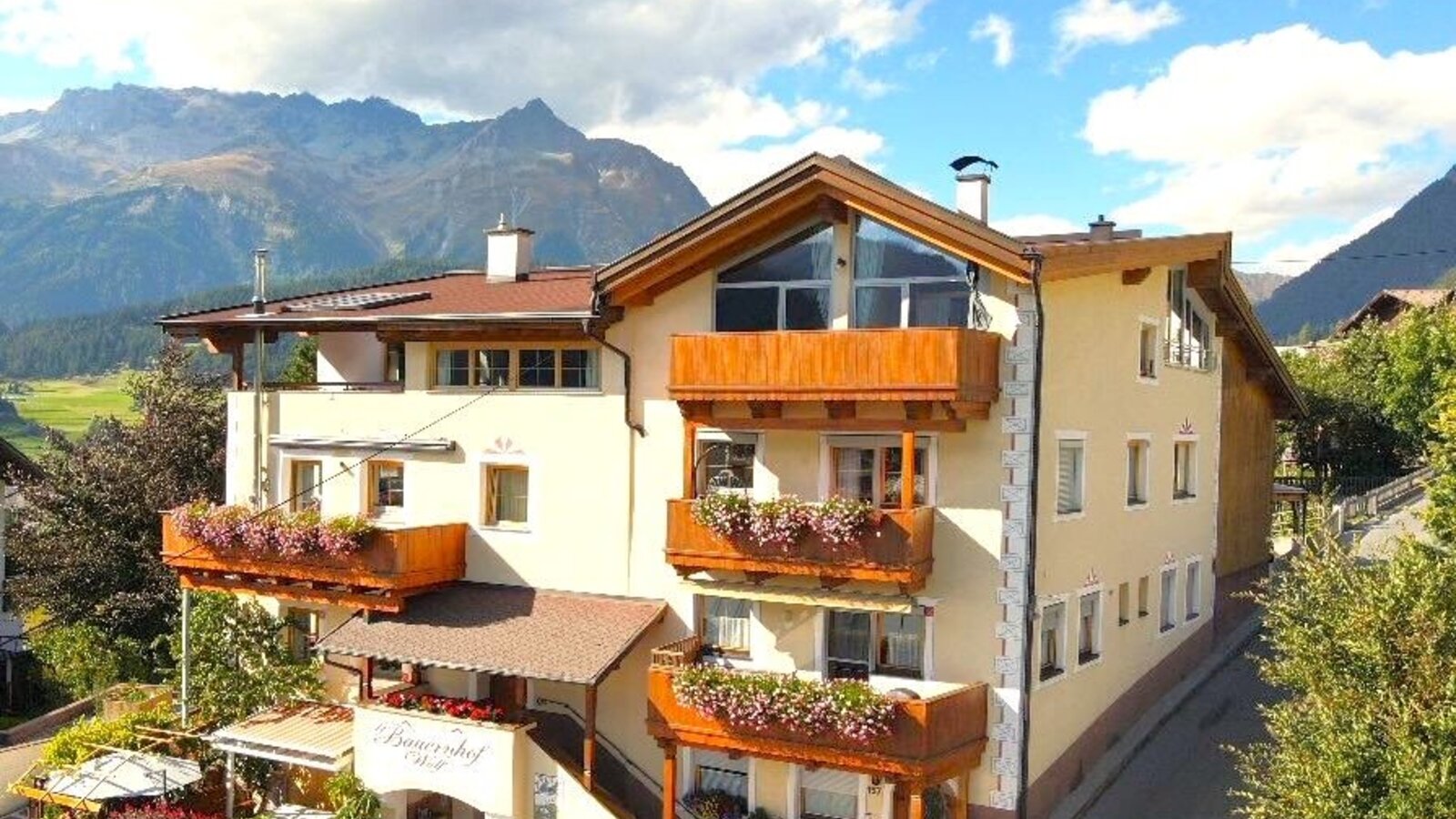 Außenansicht des Bauernhofs mit Balkonen, Blumenkästen, Sonnenterrasse und Bergblick.