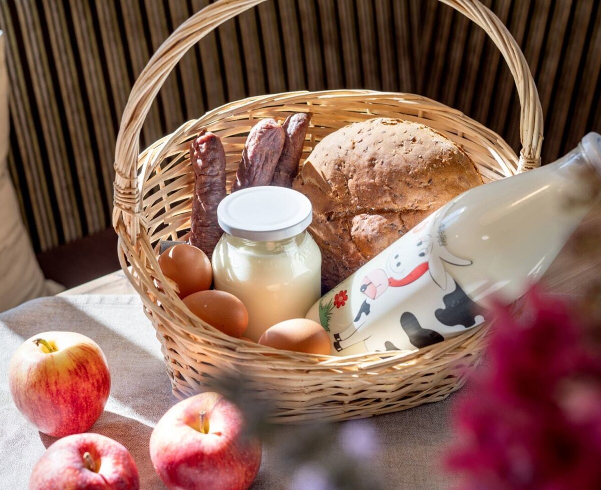 Ein einladender Korb auf dem Bauernhof, gefüllt mit frischen, hofeigenen Produkten wie Milch, Brot und Eiern.