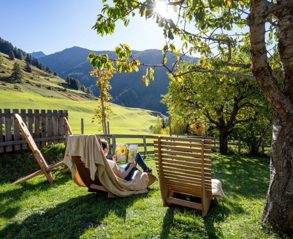 Der sonnige Garten des Bauernhofs mit hölzernen Liegestühlen und einem herrlichen Blick auf die umliegende Bergwelt.