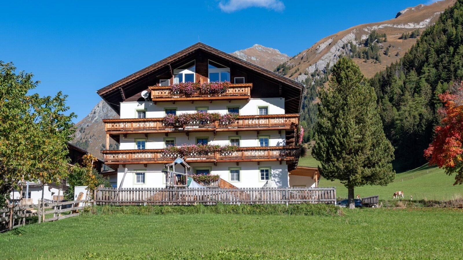 Der einladende Bauernhof mit blumengeschmückten Holzbalkonen vor der malerischen Kulisse der Osttiroler Bergwelt.