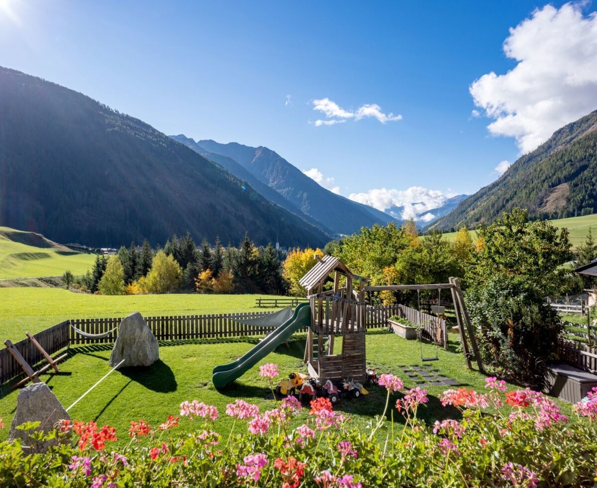 Der einladende Kinderspielplatz des Bauernhofs mit Rutsche und Schaukel vor einem idyllischen Bergpanorama.