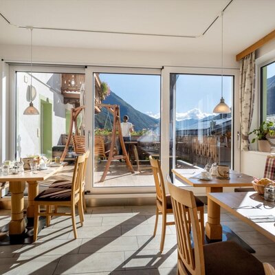 Ein lichtdurchfluteter Frühstücksraum im Bauernhof mit gemütlichen Holztischen und einem herrlichen Blick auf die umliegenden Berge.