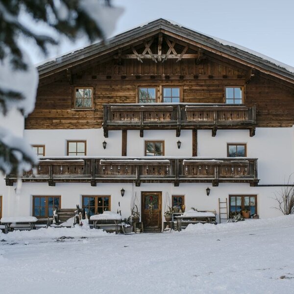 Der Bauernhof im Winter mit schneebedeckter Fassade und Holzbalkonen.