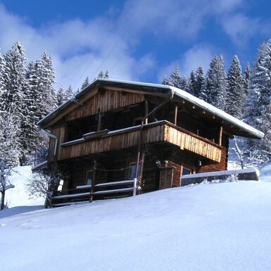 Die Alm im Winter, umgeben von Schnee und verschneiten Wäldern.