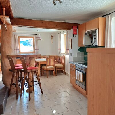 Die Alm verfügt über eine Küche mit Holzeinbauten, Herd und Mikrowelle, einen Essbereich mit Holztisch und Eckbank sowie einen Barbereich mit Barhockern.