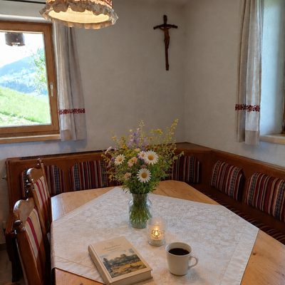 Eine gemütliche Essecke in der Hütte mit einer traditionellen Eckbank, frischen Wildblumen und einem einladend gedeckten Holztisch.