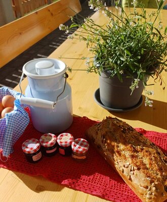 Ein reichhaltiges Alm-Frühstück mit frischem Brot, Eiern, Marmeladen und Milch auf einem sonnigen Holztisch.