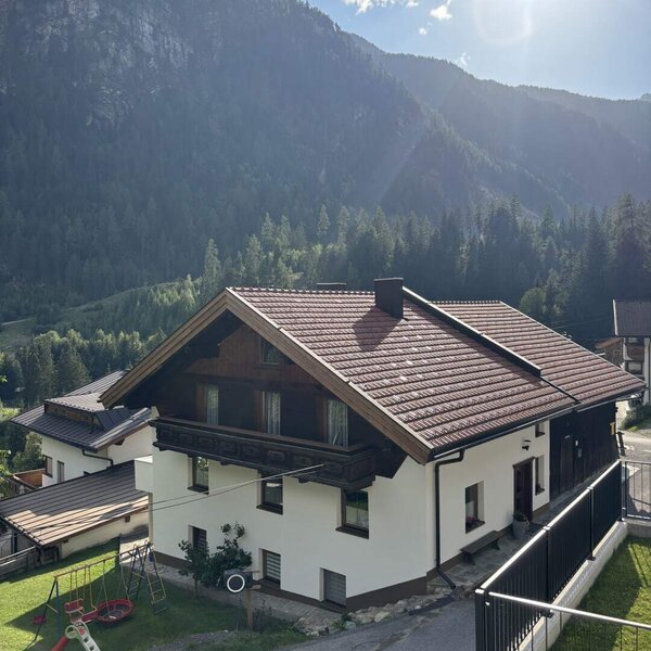 Das einladende Appartementhaus vor einer malerischen Bergkulisse mit einem kleinen Spielplatz im Garten.