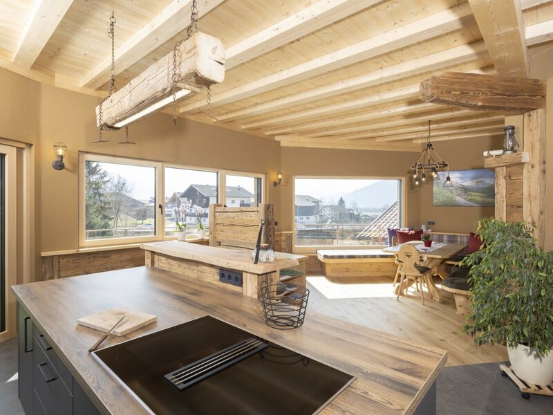 Die offene Wohnküche im Bauernhof verfügt über eine Kochinsel mit Kochfeld, einen Essbereich mit Holztisch und großen Fenstern mit Bergblick.