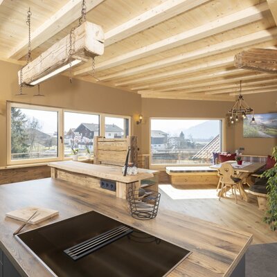Die offene Wohnküche im Bauernhof verfügt über eine Kochinsel mit Kochfeld, einen Essbereich mit Holztisch und großen Fenstern mit Bergblick.