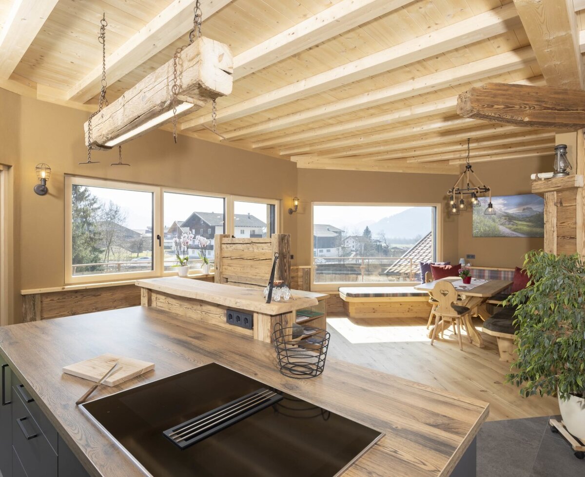 Die offene Wohnküche im Bauernhof verfügt über eine Kochinsel mit Kochfeld, einen Essbereich mit Holztisch und großen Fenstern mit Bergblick.