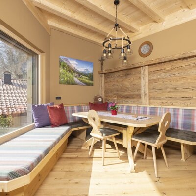 Essbereich im Bauernhof mit Holztisch, Eckbank und einer Sitzgelegenheit an der breiten Fensterfront für viel Tageslicht.