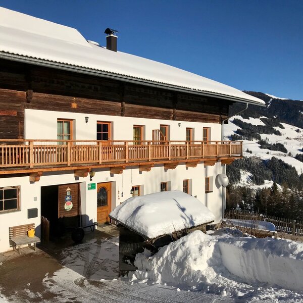 Der Bauernhof im Winter, mit Holzbalkonen und einer weiten Aussicht auf die verschneite Bergwelt.